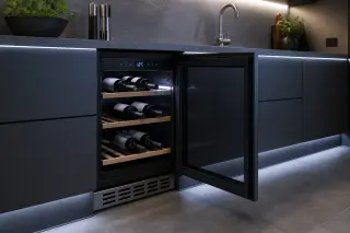 Built-in wine cooler under a modern kitchen countertop, cool LED lighting, a few unlabeled bottles inside, digital thermometer visible.