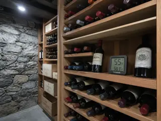 Stone vaulted wine cellar with LED lighting, neat wooden racks holding wine bottles, and a digital hygrometer placed between bottles on a shelf.