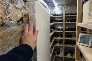 Hand checking a digital hygrometer inside a used wine fridge with a few bottles, neutral modern kitchen background, focus on practical inspection.